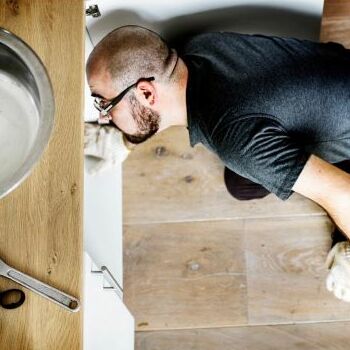 A residential plumber checks under a sink.